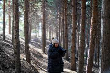 Chica joven guapa en un bosque de arboles altos con c&aacute;mara de foto colgada al cuello