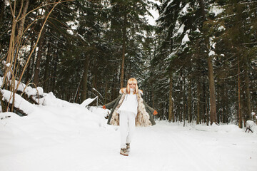 Young woman dancing in coniferous winter forest with snow, wearing white costume, fur parka jacket,...