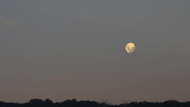 Full moon timelapse moving higher into the sky during dusk evening light.