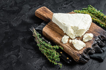 Fresh Soft goat cheese on a cutting board with thyme. Black background. Top view. Copy space