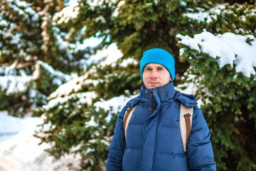 Fototapeta na wymiar Young man with backpack standing in a forest with snow-covered fir trees on a sunny winter day