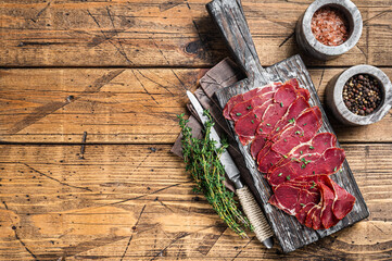 Dried Pastrami slices, beef meat with herbs on wooden board. Wooden background. Top view. Copy space