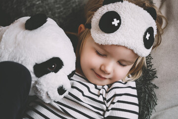 Cute little girl hugging with soft big plush panda at home. Concept of family, healthy sleep of...