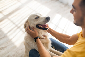 Best friend concept. Millennial Arab man scratching his dog on floor at home, selective focus