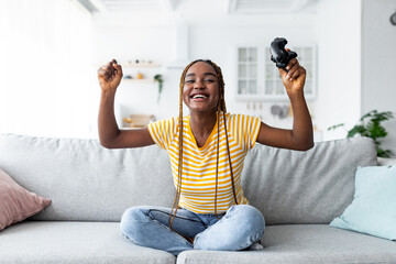 Fototapeta na wymiar Emotional young black woman winner playing video games at home