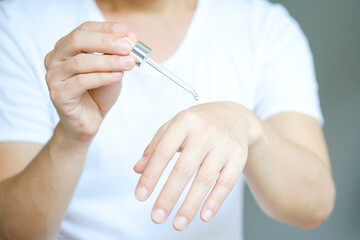 Young man's hand He drops the Collagen Moisturizer serum on his hands, and Protector skin Treatment facial essence oil, Vitamin C. Beauty and spa Concept.