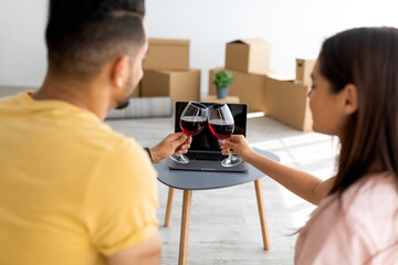 Diverse young couple celebrating housewarming party, drinking wine while speaking to friends or...
