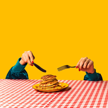 Naklejki Food pop art photography. Female hand and sweet pancakes on plaid tablecloth isolated on bright yellow background. Vintage, retro style