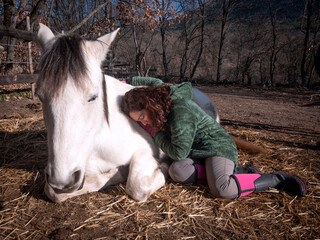 Low angle view of female in green polar fleece jacket hugging a white pony.