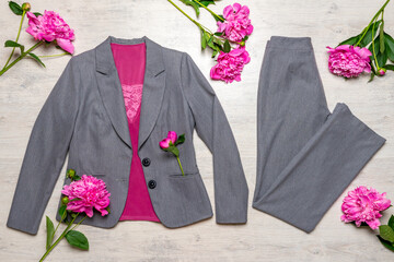 Women classic suit in grey color with pink accessories and flowers on light wooden background. Jacket and trousers with blouse and spring flowers. Beautiful stylish clothes, fashionable outfit