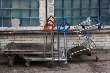 piled dirty rusty weathered cargo trolleys and standing outside on a soviet blue glass bricks windows background
