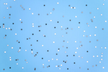 Silver stars glittering confetti on blue background. Trendy festive holiday backdrop. Many star-shaped particles for a postcard, invintation or web banner