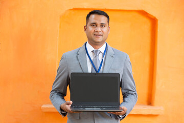 Portrait of handsome indian man wearing suit and id card showing empty laptop display screen. 