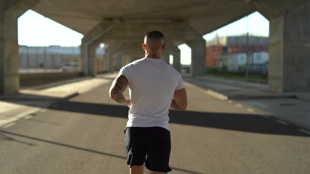 Chico joven atractivo tatuado con camiseta blanca corriendo por la carretera 