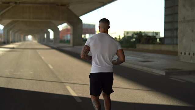 Chico joven atractivo tatuado con camiseta blanca corriendo por la carretera 