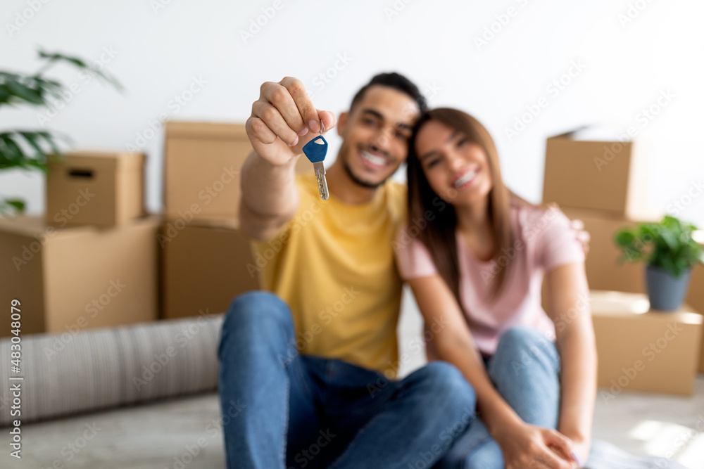 Sticker positive young multiracial couple showing house key, sitting on floor of new home, selective focus