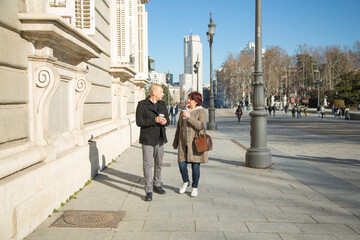 senior Caucasian couple strolling with a paper cup with coffee