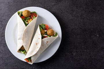 Tortilla wrap with falafel and vegetables on black background. Top view. Copy space