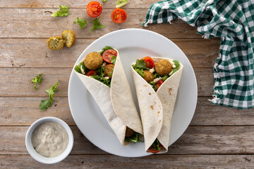 Tortilla wrap with falafel and vegetables on wooden table. Top view