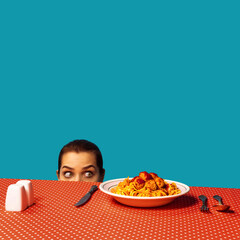 Young girl spying on spaghetti with meatballs on plaid tablecloth isolated on bright blue...