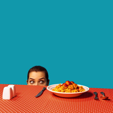 Naklejki Young girl spying on spaghetti with meatballs on plaid tablecloth isolated on bright blue background. Food pop art photography. Vintage, retro style interior