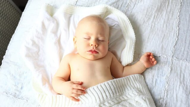 An authentic close-up of a cute Caucasian little baby boy sleeping sweetly in a comfortable white sheet. Child care, Sleeping child, Childhood, Fatherhood, Life concept
