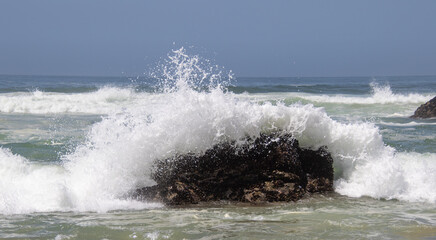 Wave breaks over a large dark rock in the ocean