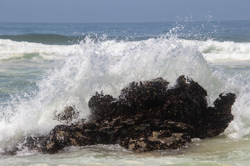 Wave breaks over a large dark rock in the ocean
