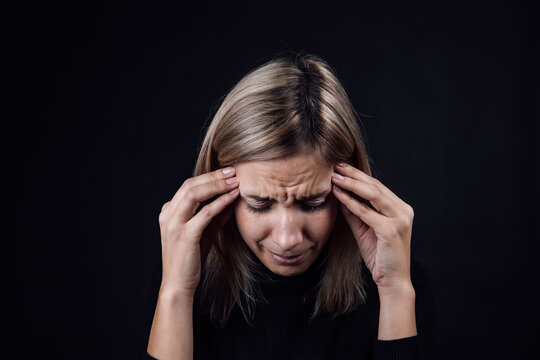 Portrait of crying woman with face down hand fingers touching temples on black background. Victim of physical and psychological abuse. Gaslighting. Relative aggression.
