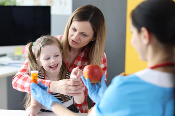 Pediatrician giving little girls choice of fruit apple or jar of vitamins in clinic