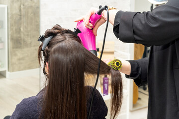 Hairdresser drying a client's hair in a beauty salon using a hair dryer and a round brush. Close-up. Copy space. High quality photo. High quality photo
