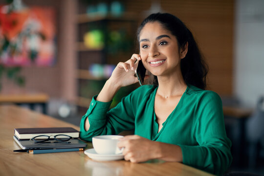 Smiling brunette indian woman drinking coffee, having phone conversation