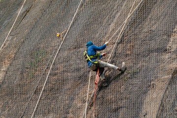 Worker at heights with no safety helmet is climbing up the landslide safety net 