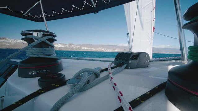 Wide shot aboard a catamaran, like all the elements that represent the sail winch, rope and sail. Filmed on Sailing Trip Santa Cruz de Tenerife In background the coast and the blue sea