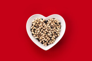 Uncooked assorted legumes in heart shape plate on red background