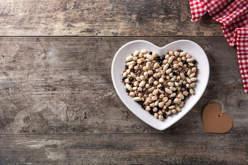 Uncooked assorted legumes in heart shape plate on rustic wooden table. Top view. Copy space