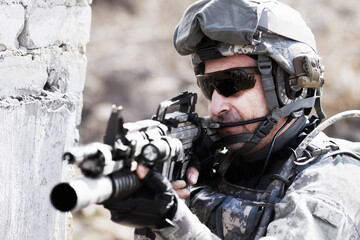 Taking aim. A soldier crouched down next to a broken down wall and pointing his gun into the...