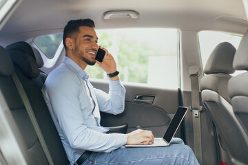 Cheerful businessman working online while going to airport by taxi