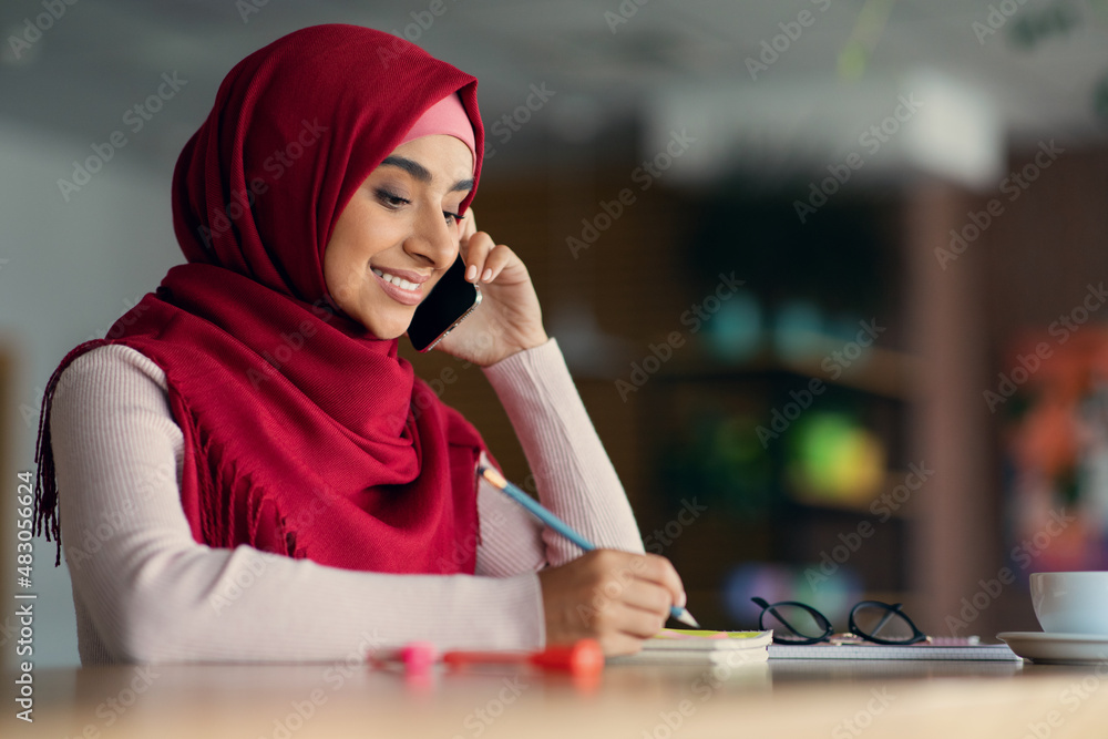 Wall mural Happy middle-eastern woman in hijab having phone conversation