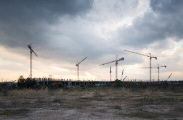 Construction site with sunset sky background at evening consist of concrete structure of building, tower crane or equipment and scaffolding. Large project to development city by engineering technology