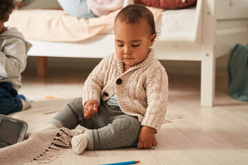 Multiracial toddler sitting at the floor and playing near his elderly brother and lovely mother