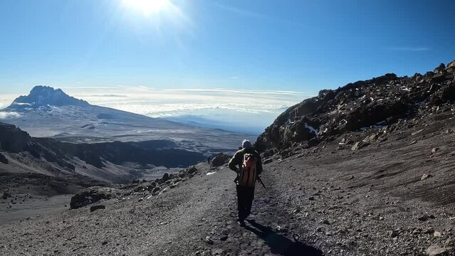The guy descends from Mount Kilimanjaro. View from the back. Beautiful mountain landscape. Mount Mawenzi in the distance. Climbing Kilimanjaro.