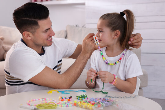 Happy father putting handmade beaded jewelry on his cute daughter at home