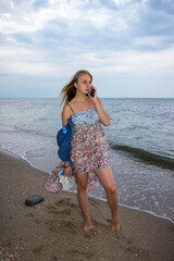 a young girl in the evening on the seashore in a sundress and with a hat   