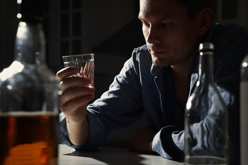 Addicted man with alcoholic drink at table in kitchen