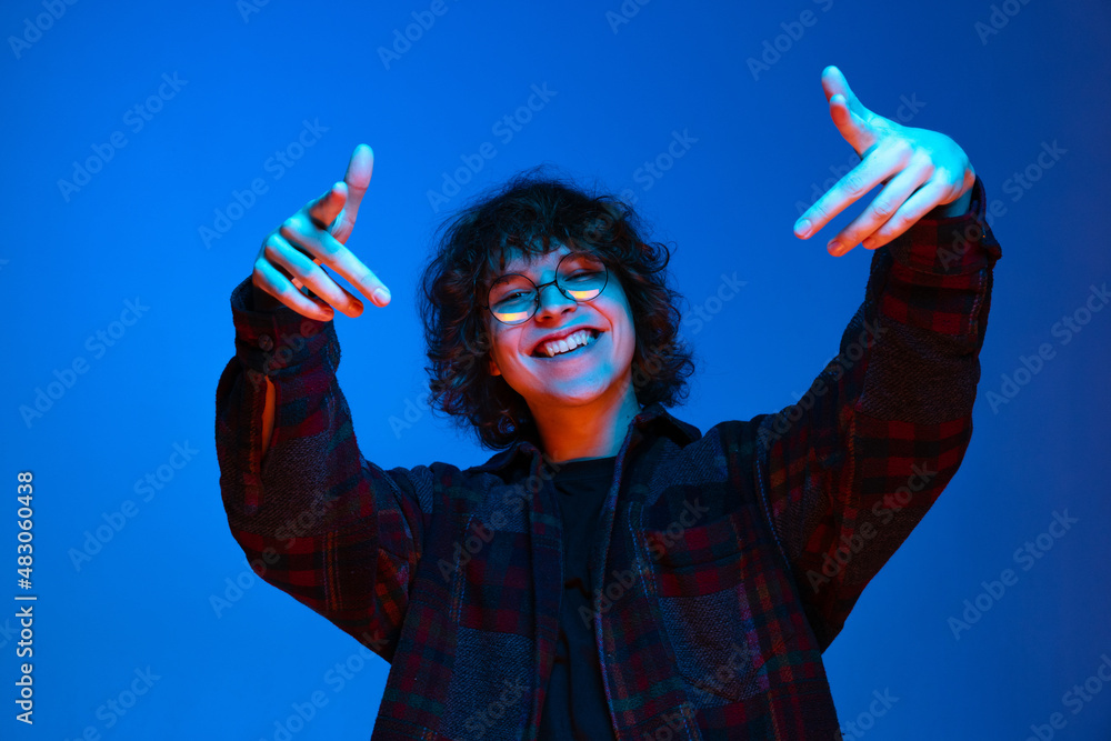 Wall mural portrait of young cheerful boy, student in black shirt isolated on dark blue background in neon ligh