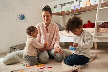 Single mother is sitting on the floor and playing with her small kids