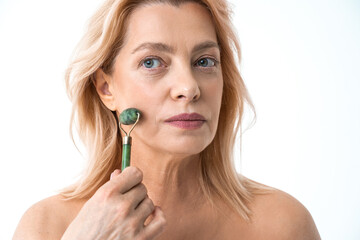 Woman standing isolated on the white background and using green quartz face roller