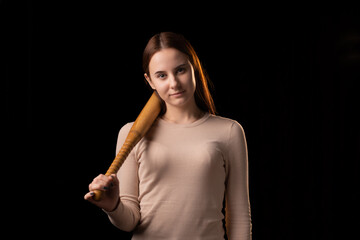 A young woman holds a bat in her hands and calmly looks into the camera. Black background....