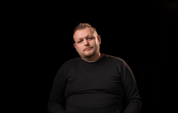 Portrait Of A Young Man With A Beard. Dark Background. A Slightly Overweight Man With A Large Build.